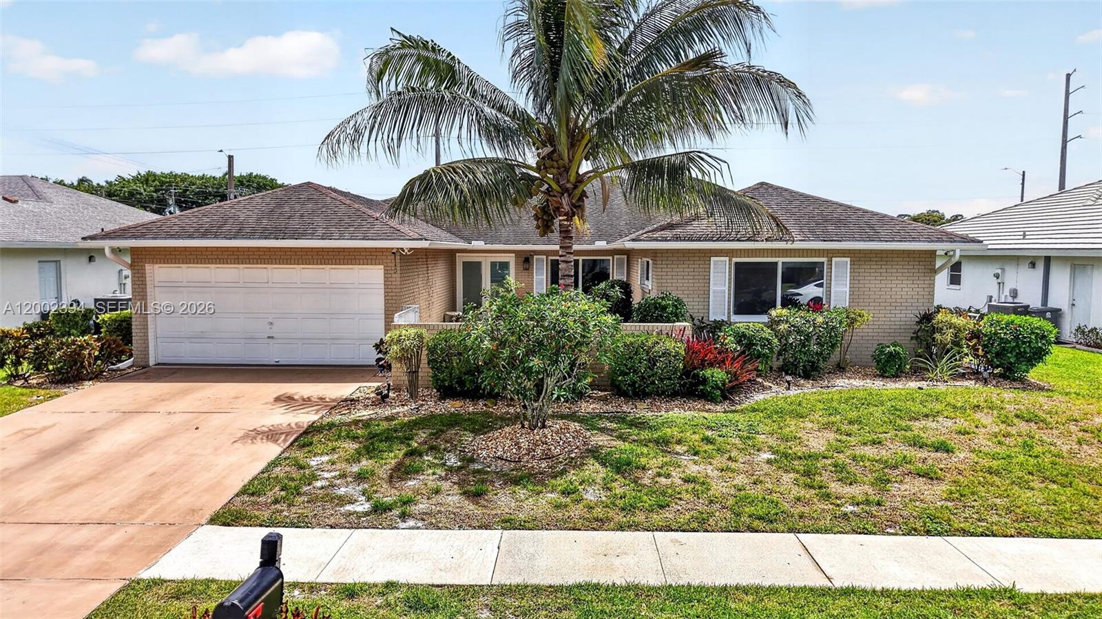 A single-story brick house features a two-car garage, a palm tree, and a front lawn — 10982 S Greentrail Dr S, Boynton Beach FL 33436, BOYNTON BEACH, FL