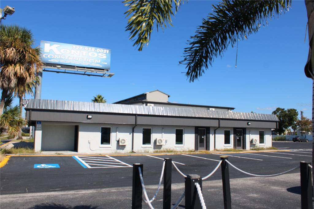 A single-story commercial building with a metal roof and a large construction company billboard — 1516-1518 US HIGHWAY 19 UNIT D, E, HOLIDAY, FL