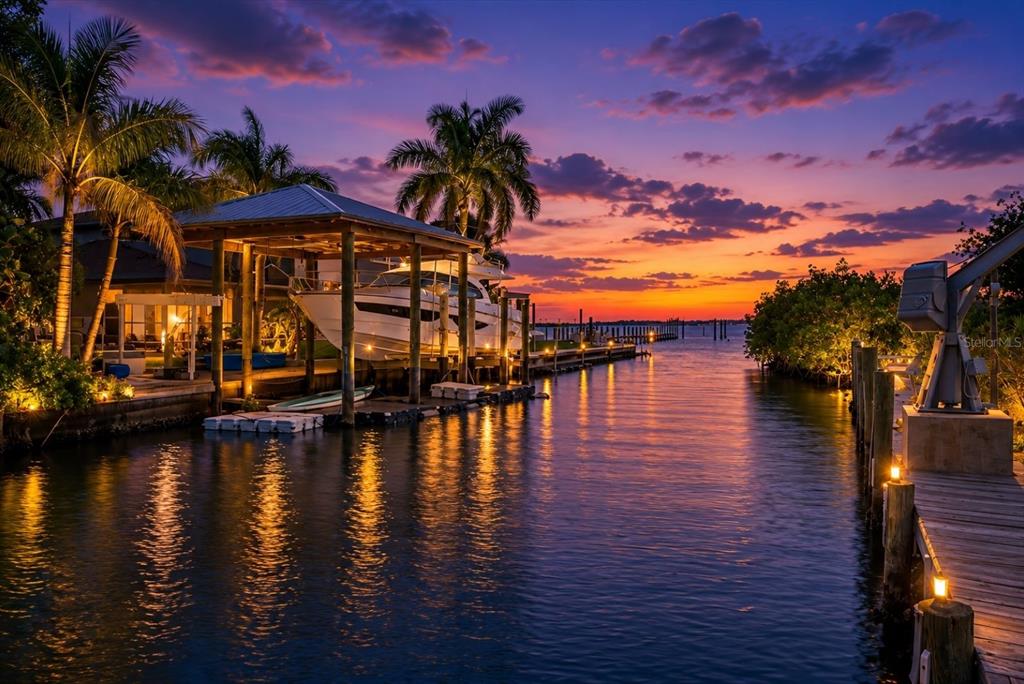 A boat is docked under a covered lift in a canal at sunset — 512 PALM AVENUE, ELLENTON, FL