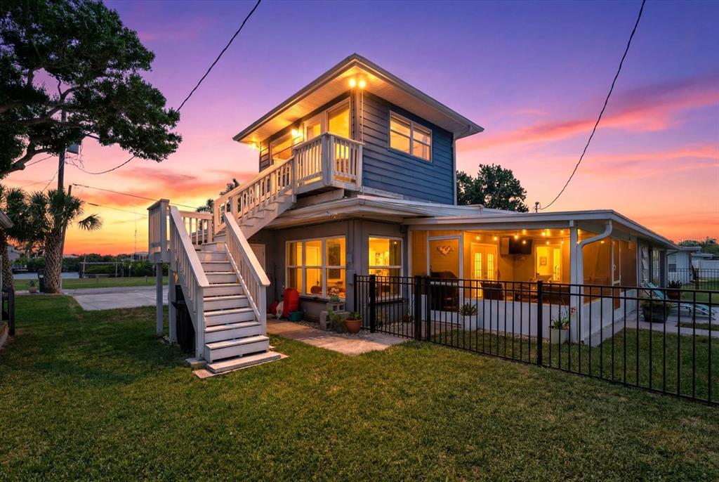A two-story house with an exterior staircase, a screened-in porch, and a fenced yard at sunset — 512 PALM AVENUE, ELLENTON, FL