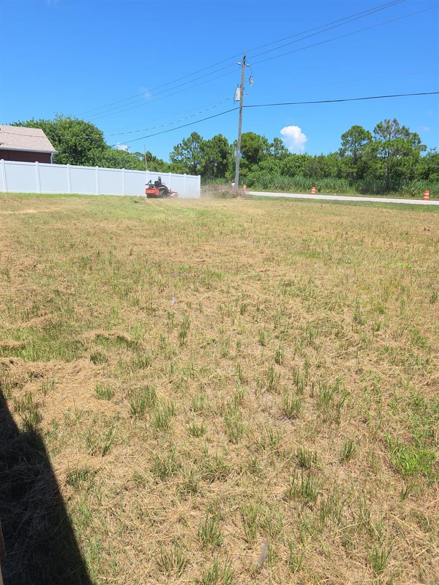 A person on a riding lawnmower cuts grass in a large, open residential lot — 8565 90th Avenue, Vero Beach FL 32967, VERO BEACH, FL