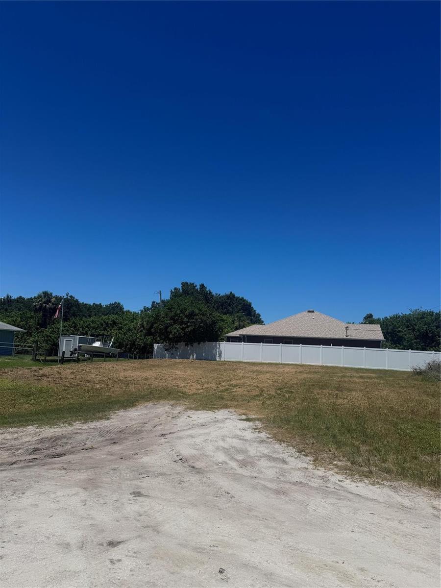 A vacant, grassy lot features a dirt driveway, a white fence, and a nearby house — 8565 90th Avenue, Vero Beach FL 32967, VERO BEACH, FL