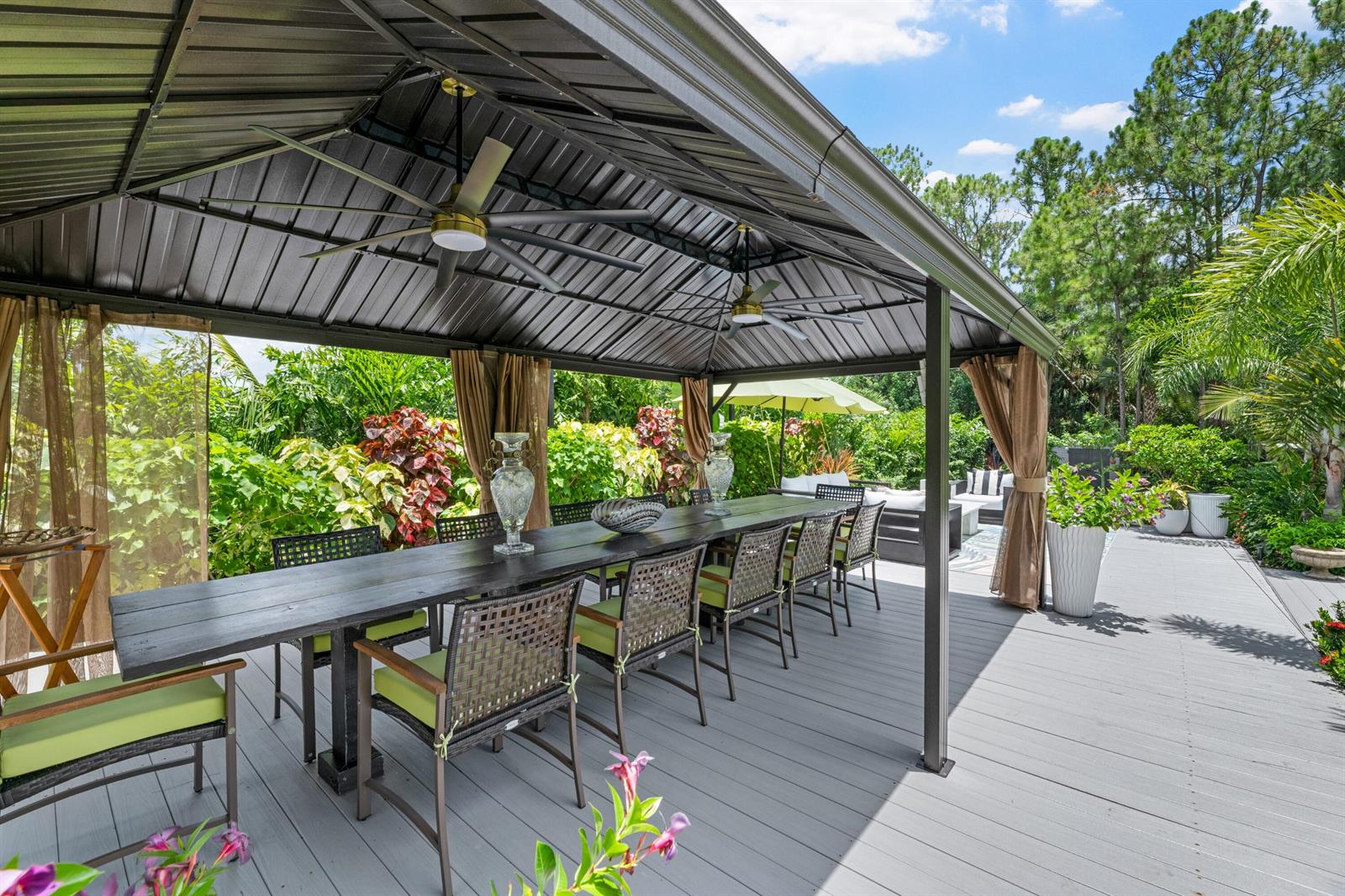 A covered outdoor dining area features a long black table with chairs on a deck — 14800 April Drive, FL 33470, FL