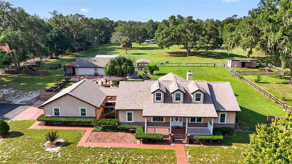 An aerial view shows a tan house with a shingled roof, dormers, and surrounding acreage — 10844 SE HIGHWAY 42, SUMMERFIELD, FL