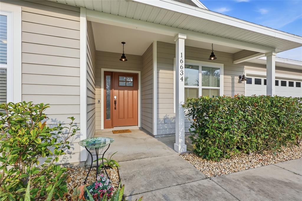 A tan house exterior features a covered porch, a brown front door, and green hedges — 16634 NW 193RD TERRACE, HIGH SPRINGS, FL