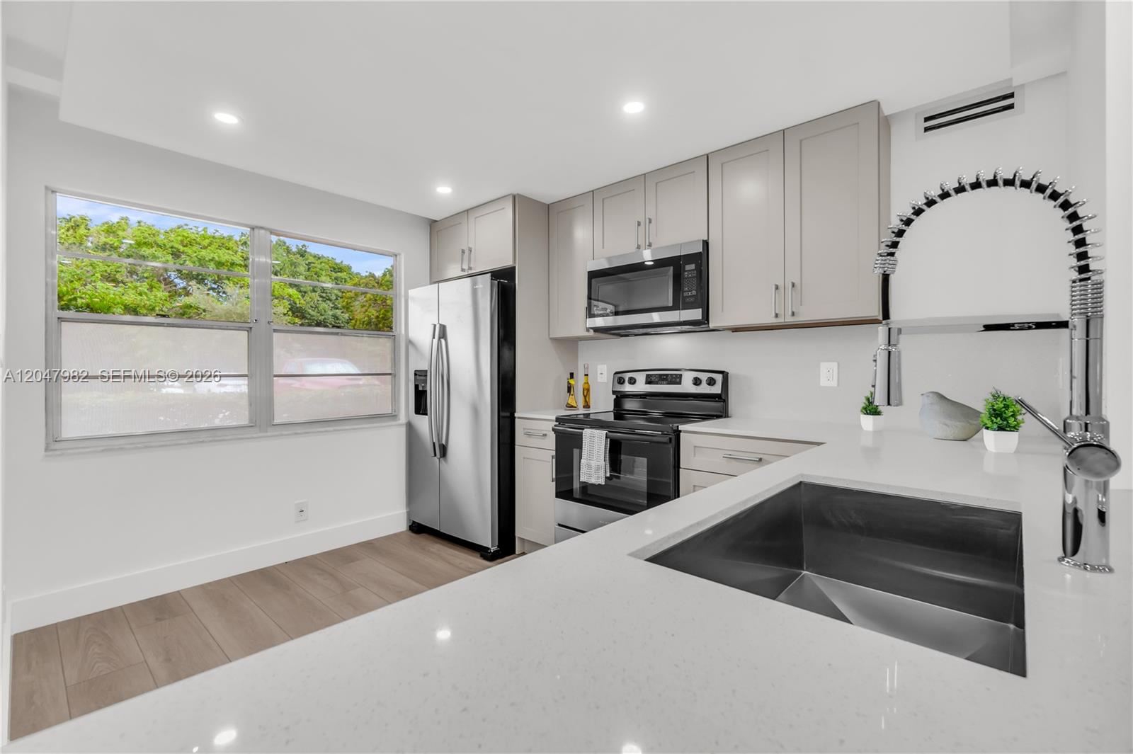 A modern kitchen features light gray cabinets, stainless steel appliances, and white quartz countertops — 2101 Lucaya Bnd # E1, Coconut Creek FL 33066, COCONUT CREEK, FL