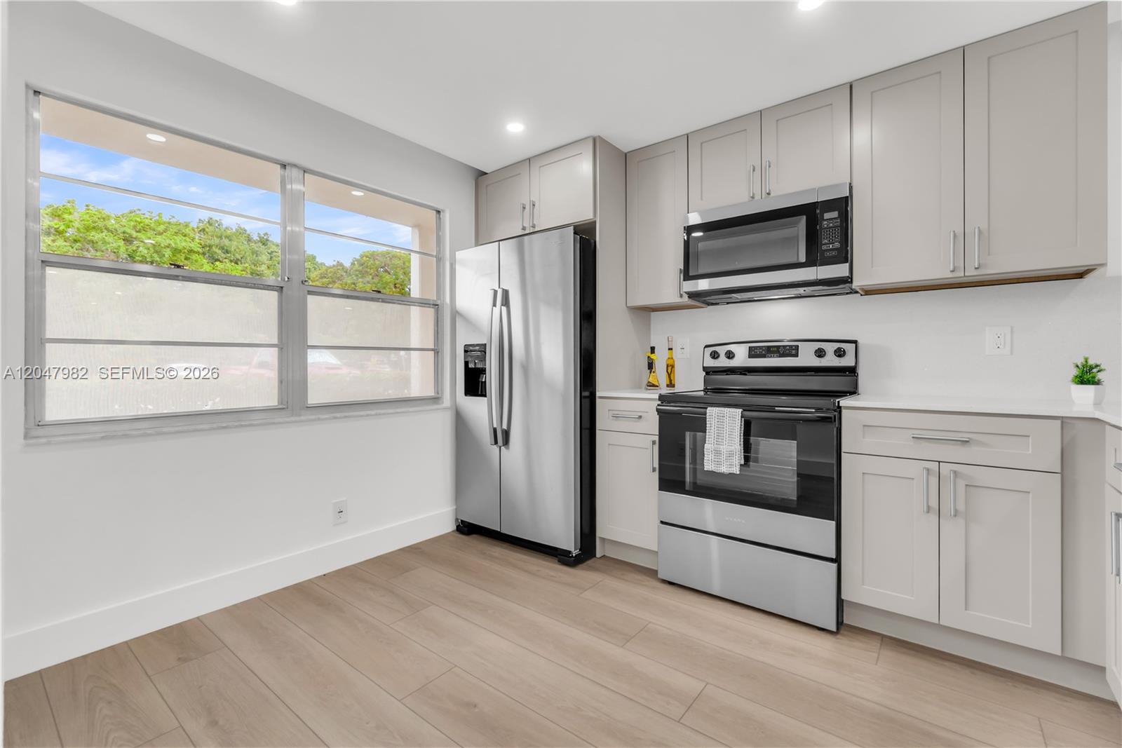 A kitchen features light gray cabinets, stainless steel appliances, white countertops, and wood-look flooring — 2101 Lucaya Bnd # E1, Coconut Creek FL 33066, COCONUT CREEK, FL