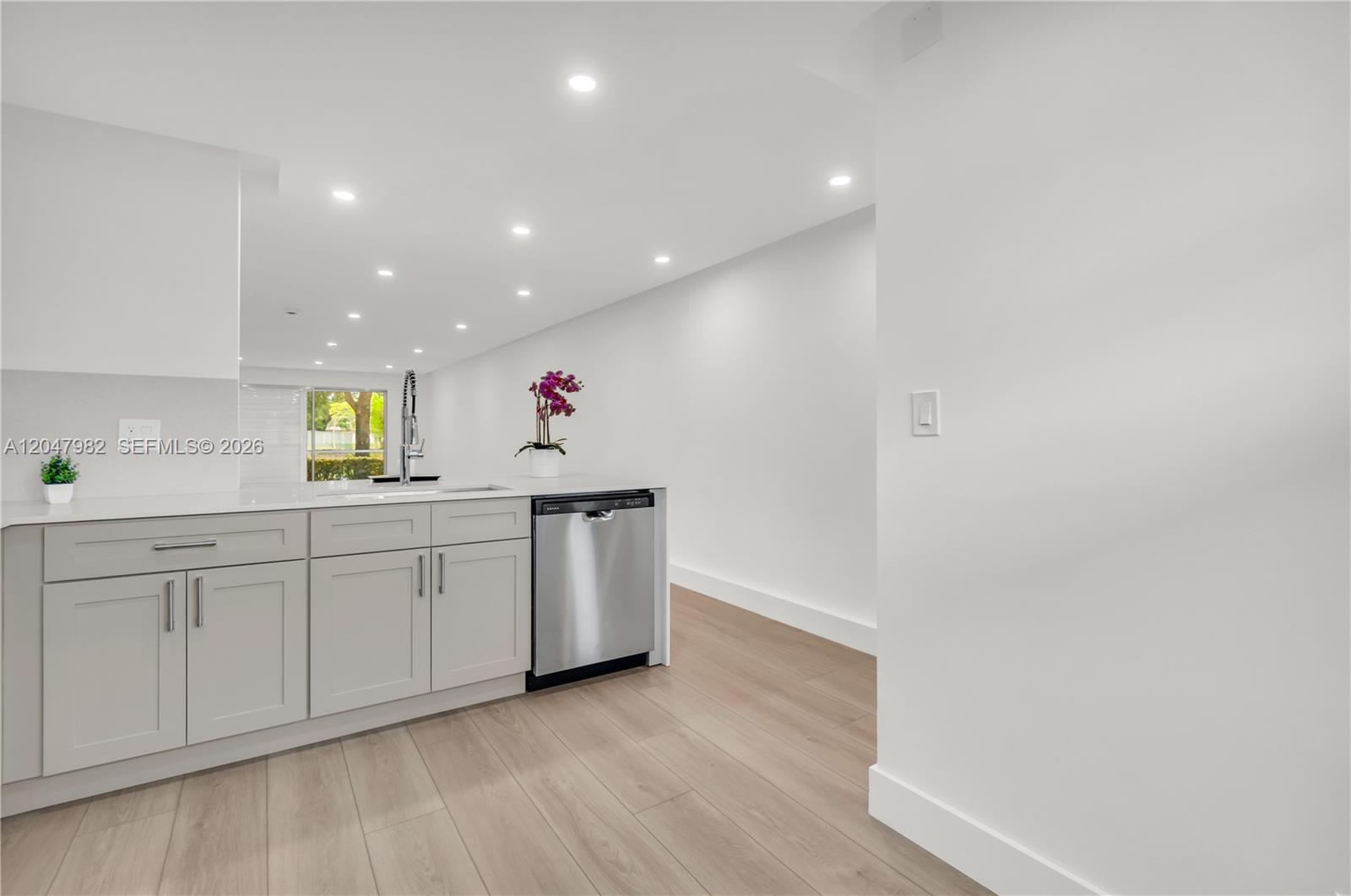 A modern kitchen features light gray cabinets, stainless steel appliances, and light wood-look flooring — 2101 Lucaya Bnd # E1, Coconut Creek FL 33066, COCONUT CREEK, FL