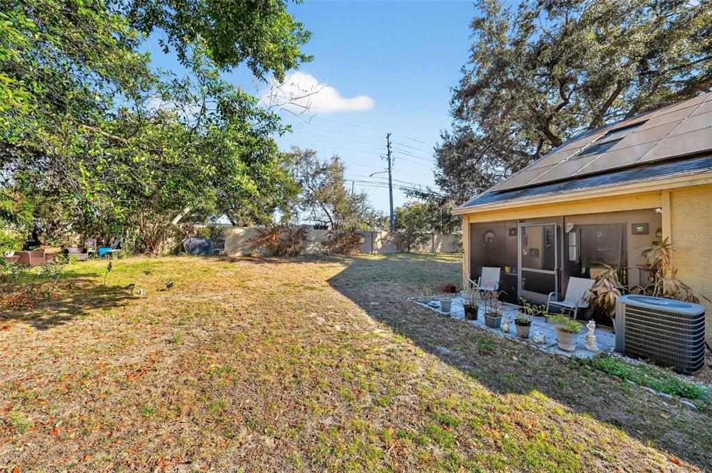 A backyard with a lawn, trees, a screened patio, and solar panels on the roof — 1300 WOODMAN WAY, ORLANDO, FL