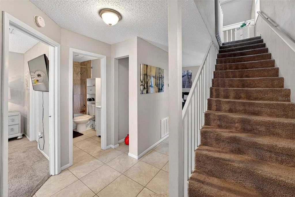 A tiled hallway features a staircase with brown carpet, a bathroom, and an adjacent bedroom — 1300 WOODMAN WAY, ORLANDO, FL
