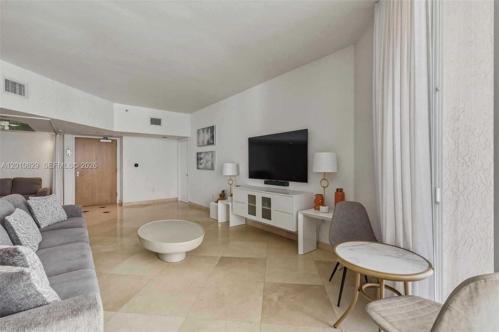 A living room features a gray sofa, a white media console, and a small table — SUNNY ISLES BEACH, FL