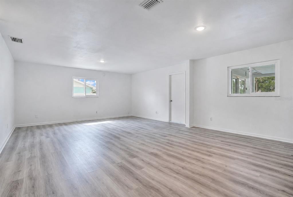 An empty room with white walls, light wood-look flooring, two windows, and a closed door — 205 FERN ROAD, WINTER HAVEN, FL