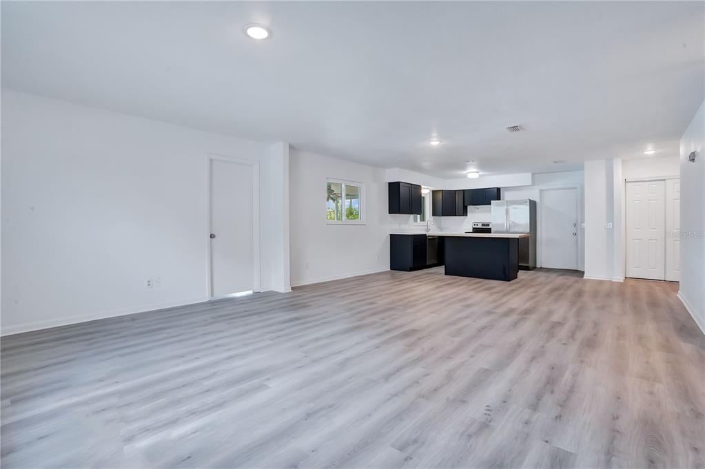 An open-concept living area features light wood-look flooring, white walls, and a modern black kitchen — 205 FERN ROAD, WINTER HAVEN, FL