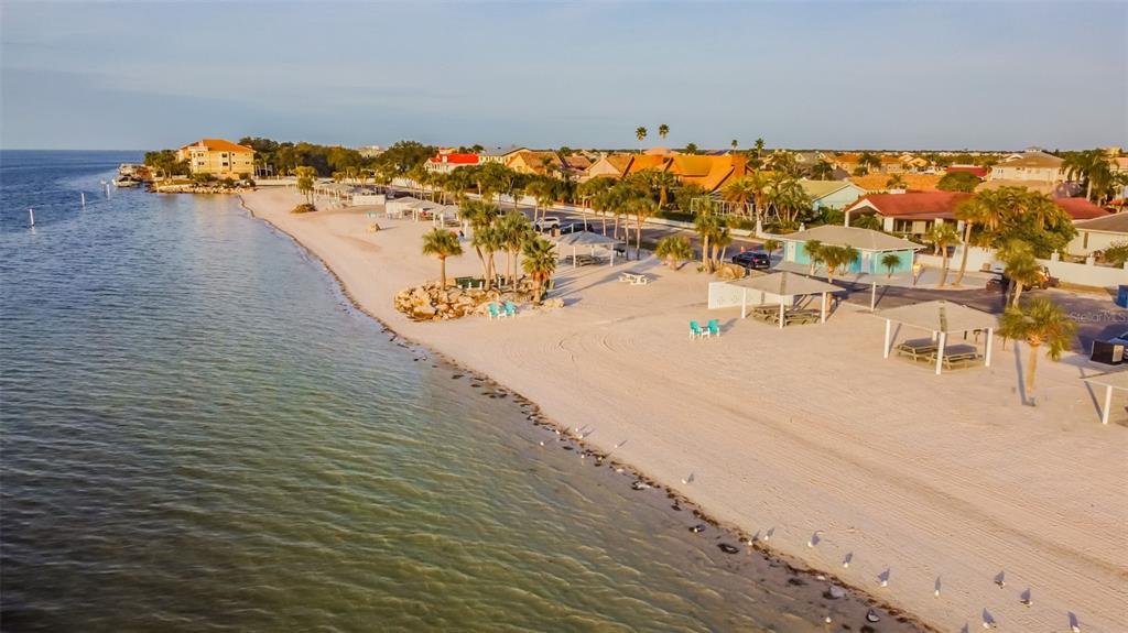 An aerial view of a sandy beach with palm trees, picnic shelters, and nearby houses — 4234 FLORAMAR TERRACE, NEW PORT RICHEY, FL