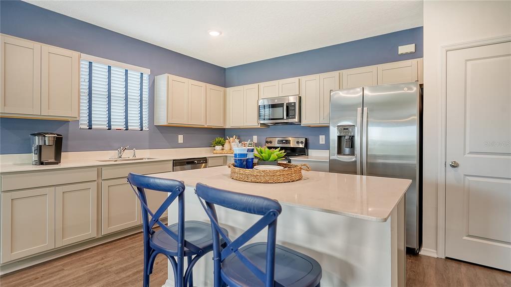 A kitchen features light-colored cabinets, stainless steel appliances, a central island, and blue accent walls — 13217 SASSAFRAS TRAIL, PARRISH, FL