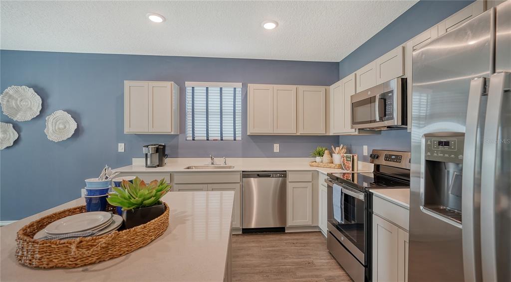 A kitchen features light-colored cabinets, stainless steel appliances, a quartz island, and blue walls — 13217 SASSAFRAS TRAIL, PARRISH, FL