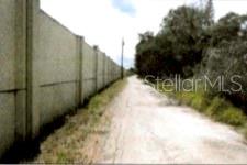 A dirt path runs alongside a tall concrete wall next to a line of trees — 12325 & 12303 STAGG ROAD, WINTER GARDEN, FL
