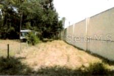 A vacant, grassy lot sits beside a tall concrete wall with trees in the background — 12325 & 12303 STAGG ROAD, WINTER GARDEN, FL