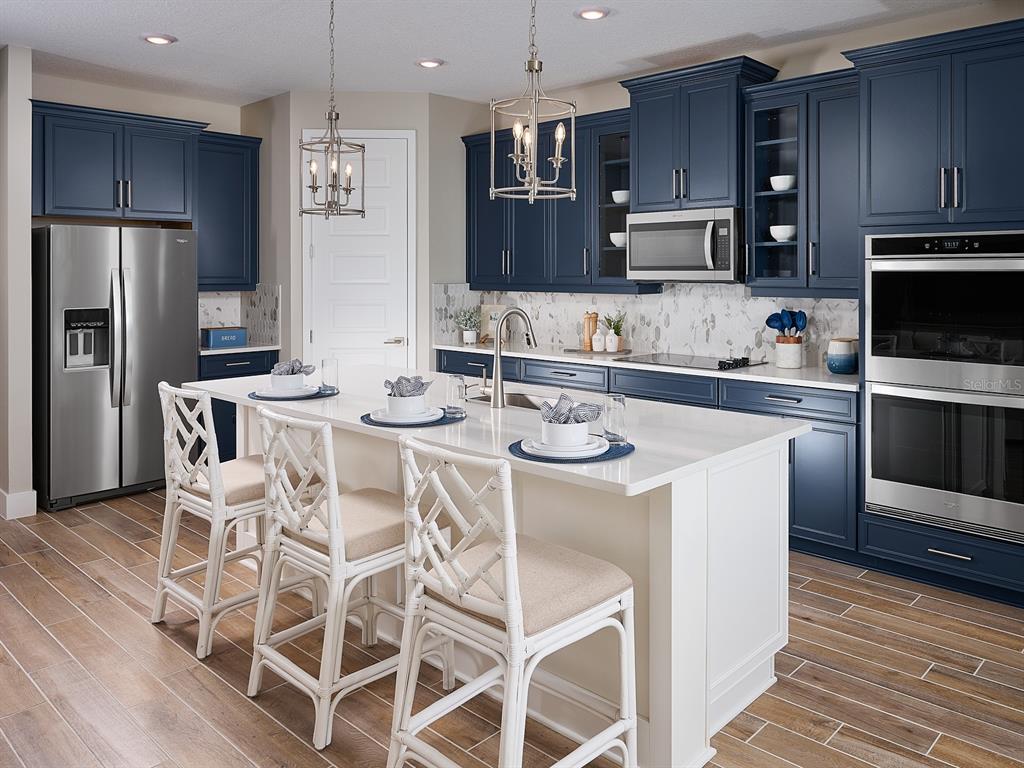 A kitchen features dark blue cabinets, a white island with three chairs, and stainless appliances — 384 BIRKDALE DRIVE, DAYTONA BEACH, FL