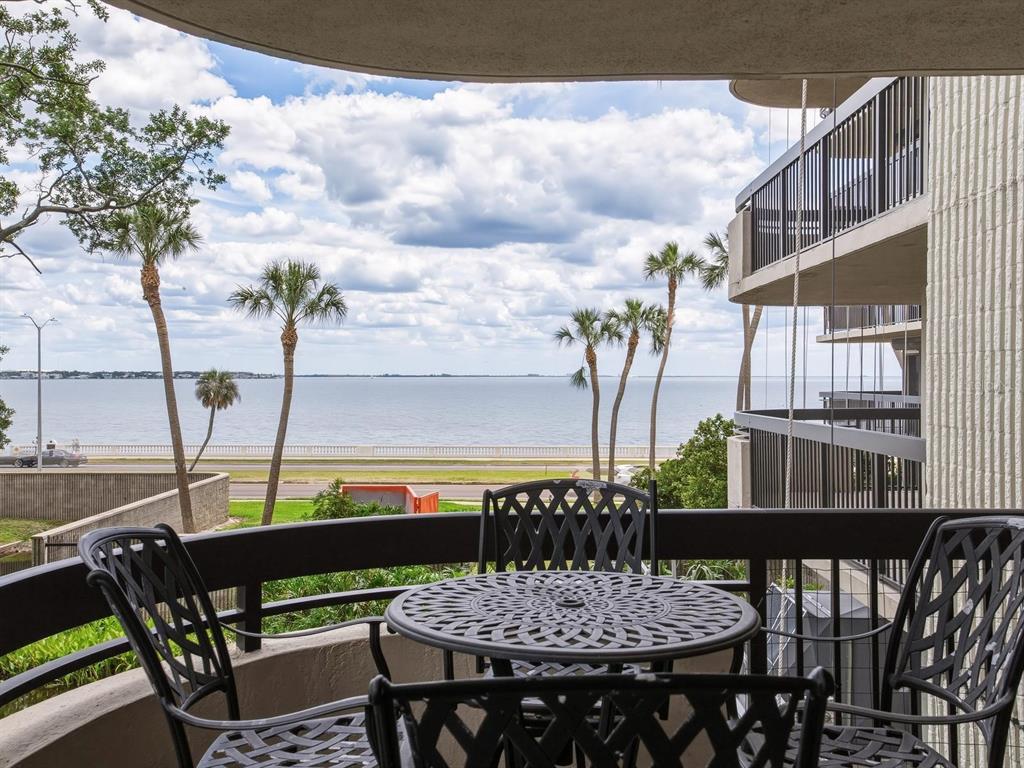 A balcony with metal furniture overlooks a waterfront view with palm trees and a cloudy sky — 2413 BAYSHORE BOULEVARD UNIT 201, TAMPA, FL