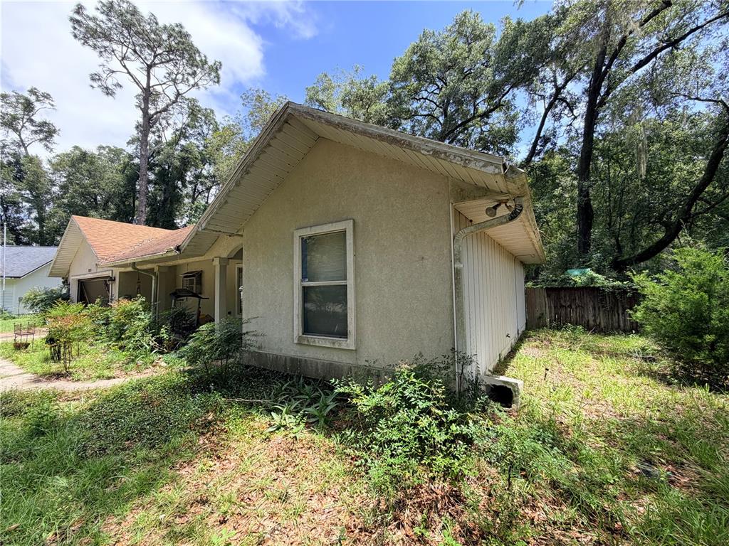 A side view of a single-story house with stucco siding, a gable roof, and overgrown landscaping — 13521 NW 137TH PLACE, ALACHUA, FL