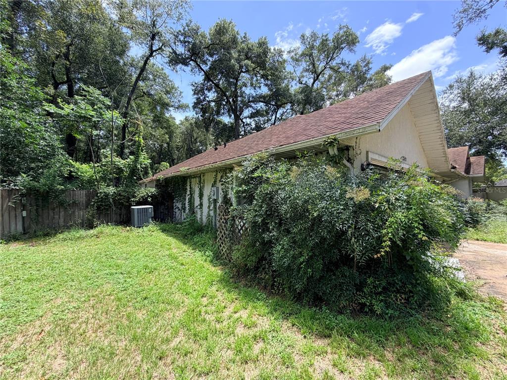 A side view of a house exterior with overgrown vegetation, a lawn, and an AC unit — 13521 NW 137TH PLACE, ALACHUA, FL