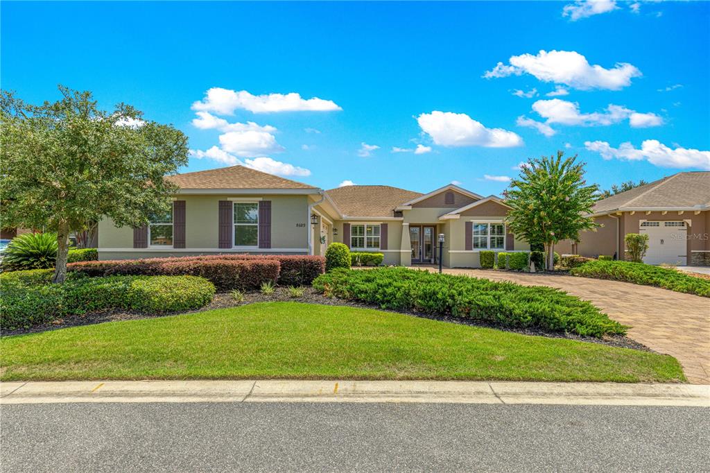 A single-story house with a paved driveway, tan stucco exterior, and a manicured front lawn — 8689 SW 93RD CIRCLE, OCALA, FL