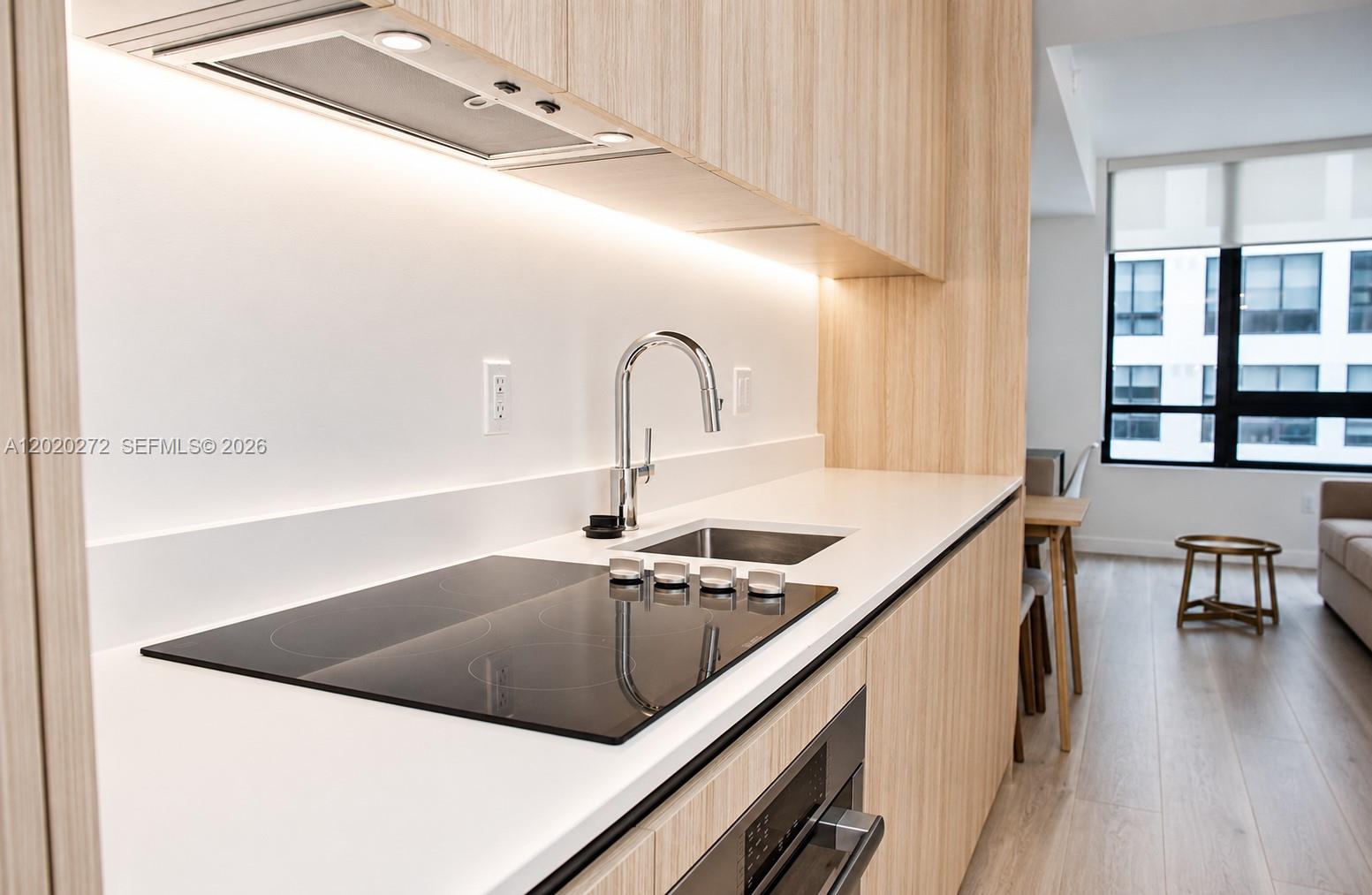 A modern kitchen features light wood cabinetry, a white countertop, and a black induction cooktop — 225 N Miami Ave # 2308, Miami FL 33128, MIAMI, FL