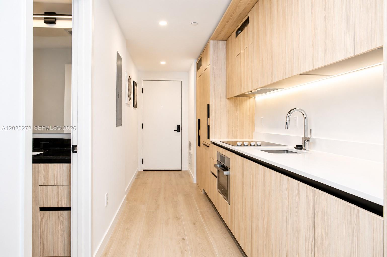 A modern galley kitchen features light wood cabinetry, white countertops, and stainless steel appliances — 225 N Miami Ave # 2308, Miami FL 33128, MIAMI, FL