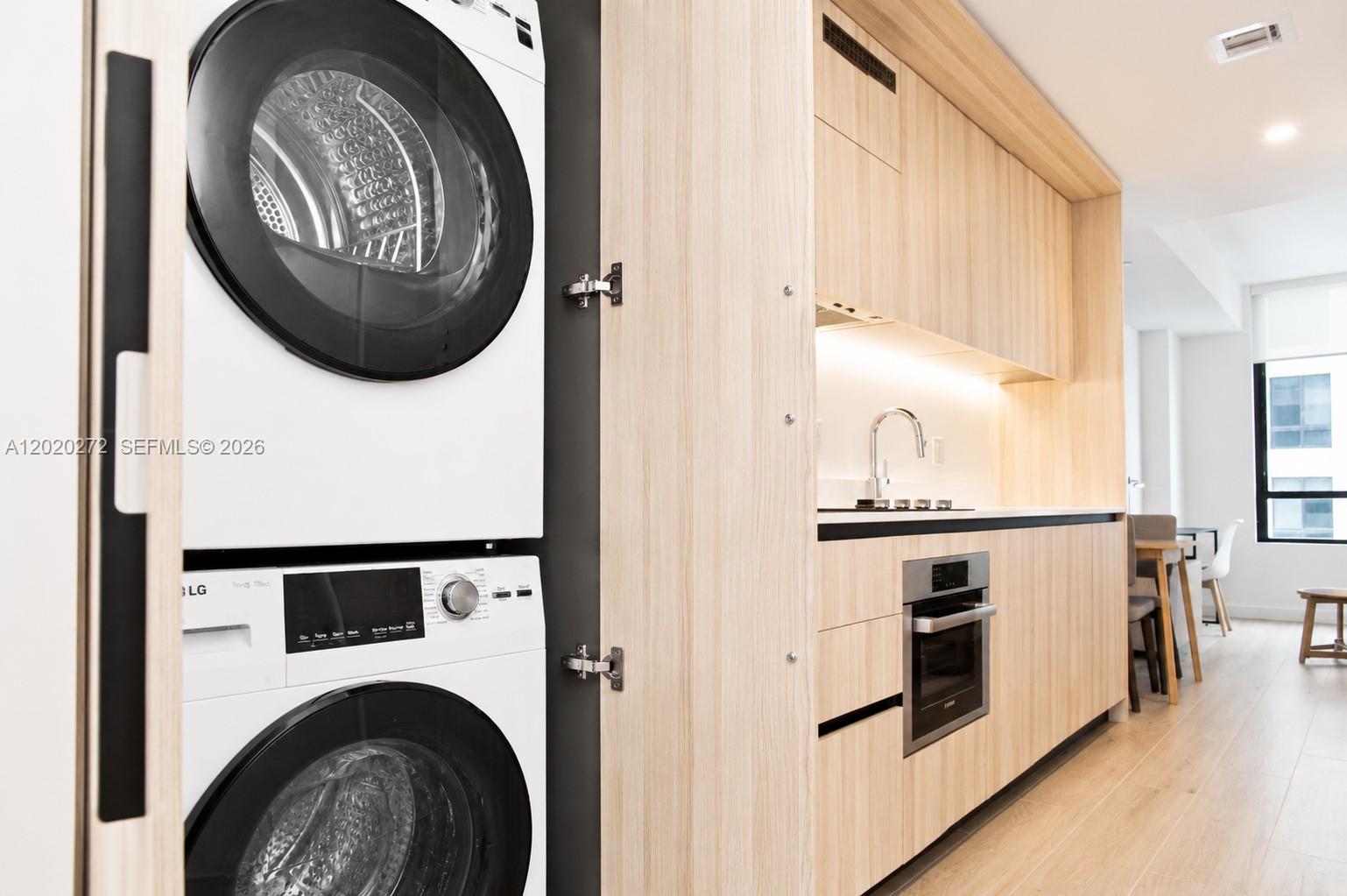A stacked LG washer and dryer unit sits beside a modern kitchen with light wood cabinetry — 225 N Miami Ave # 2308, Miami FL 33128, MIAMI, FL