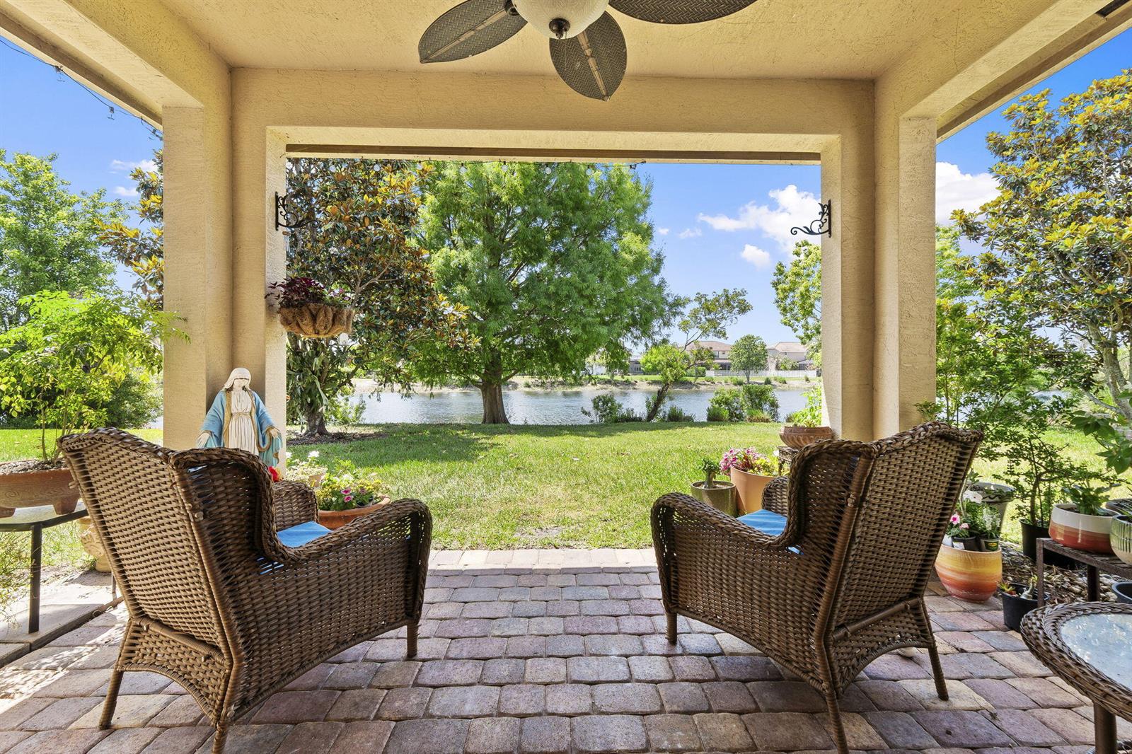 A covered patio with wicker chairs overlooks a grassy backyard and a lake — 1428 SE Summit Trail, Stuart FL 34997, STUART, FL