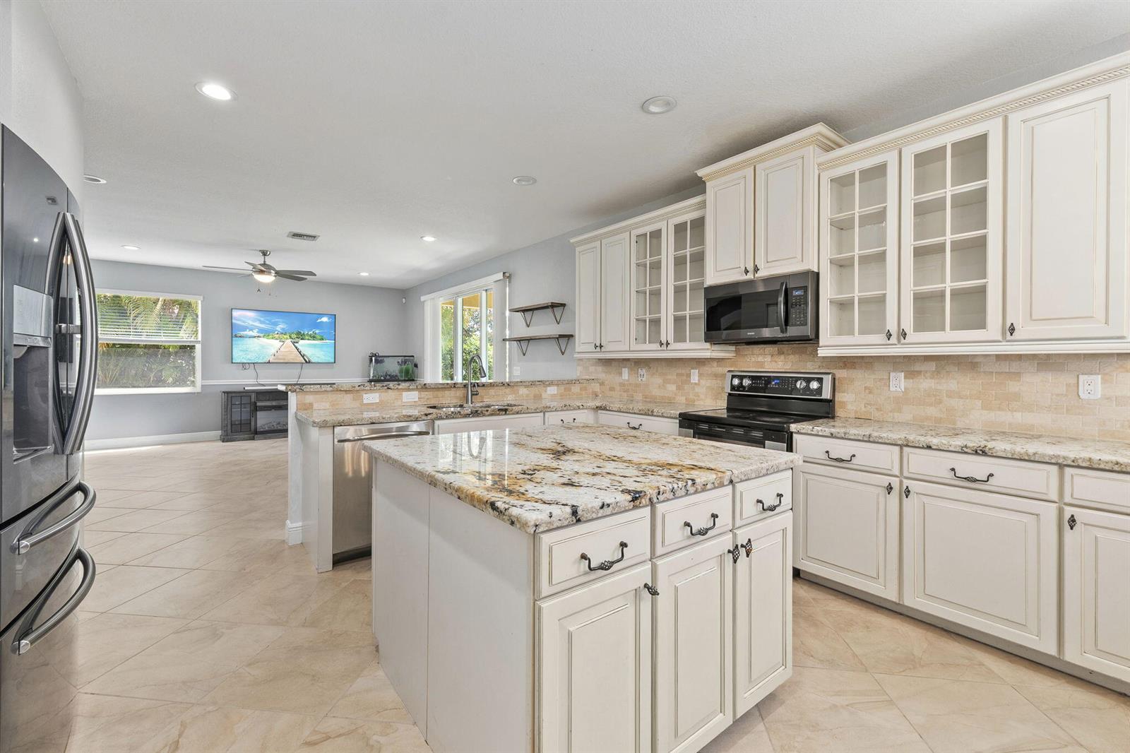 A kitchen with white cabinets, granite countertops, and an island opens to a living area — 1428 SE Summit Trail, Stuart FL 34997, STUART, FL