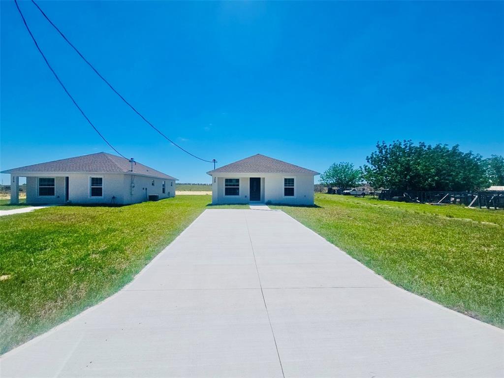 Two single-story houses with concrete driveways stand on a grassy lot under a clear sky — 328 MOUNTAIN DRIVE, BABSON PARK, FL