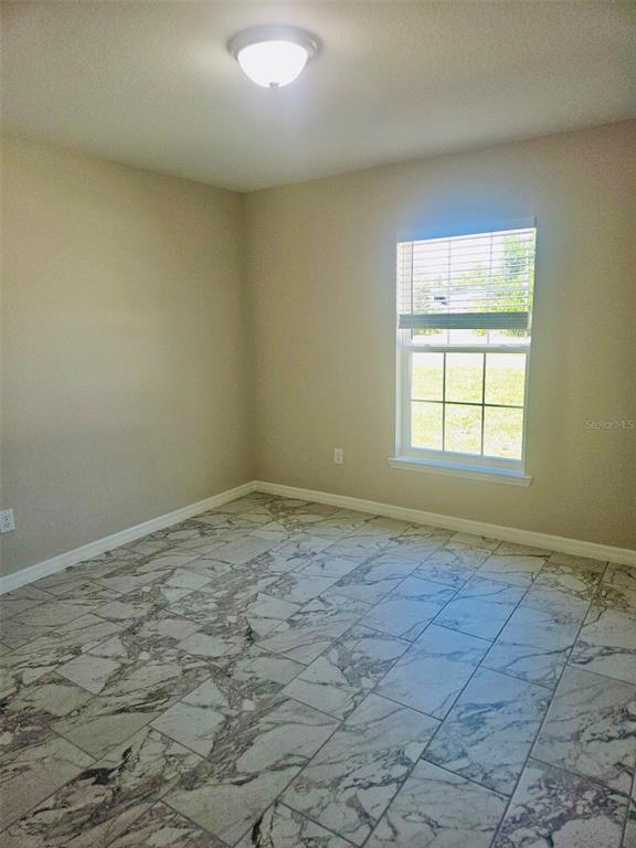 An empty room with beige walls, a single window, and patterned marble-look tile flooring — 328 MOUNTAIN DRIVE, BABSON PARK, FL