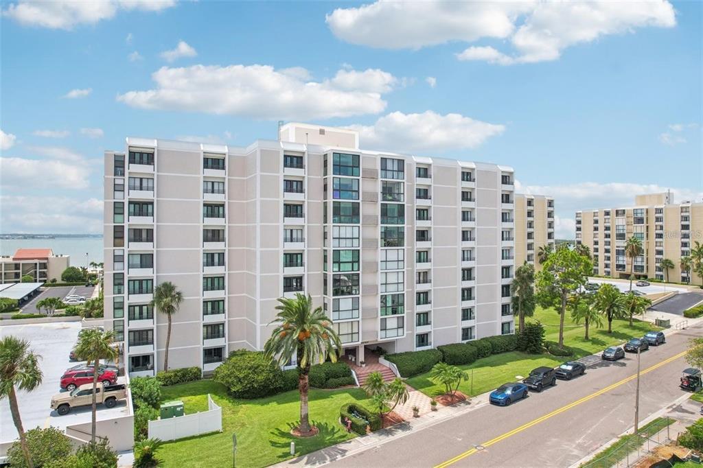 An exterior view of a multi-story apartment building with palm trees and a parking lot — 851 BAYWAY BOULEVARD UNIT 103, CLEARWATER BEACH, FL