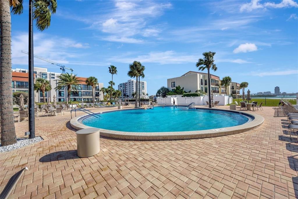 A circular swimming pool sits on a paved patio surrounded by palm trees and buildings — 851 BAYWAY BOULEVARD UNIT 103, CLEARWATER BEACH, FL