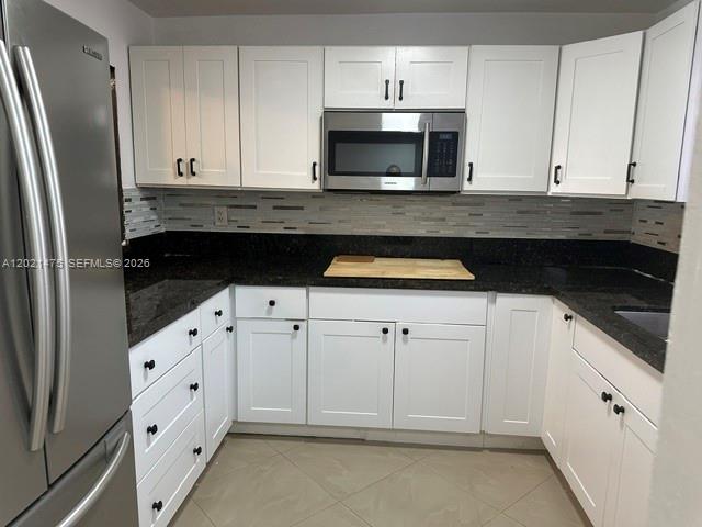 A kitchen features white cabinets, dark countertops, a stainless steel microwave, and a tile backsplash — 6175 W 20th Ave # 309, Hialeah FL 33012, HIALEAH, FL