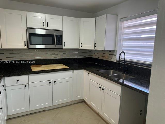 A kitchen features white cabinets, dark granite countertops, a stainless steel microwave, and a window — 6175 W 20th Ave # 309, Hialeah FL 33012, HIALEAH, FL