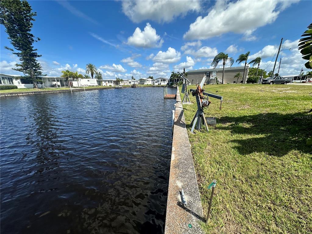 A concrete seawall borders a canal next to a grassy lot with a boat lift — 506 CLARION PLACE, NORTH PORT, FL