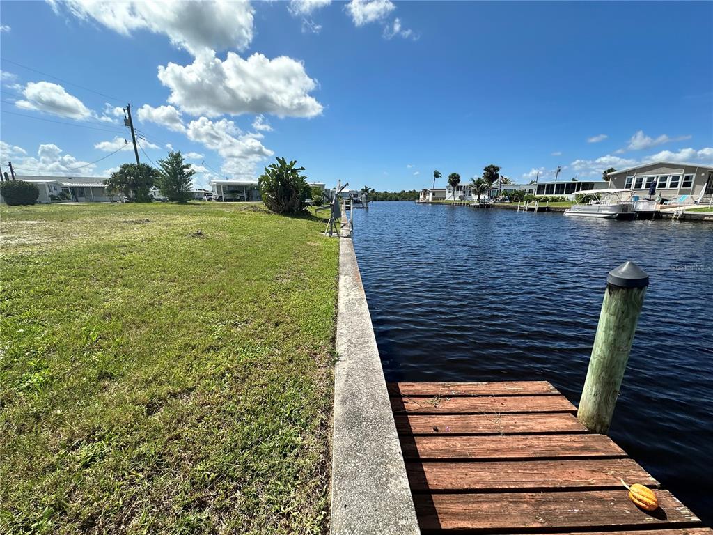 A grassy waterfront lot features a concrete seawall and a small wooden dock — 506 CLARION PLACE, NORTH PORT, FL