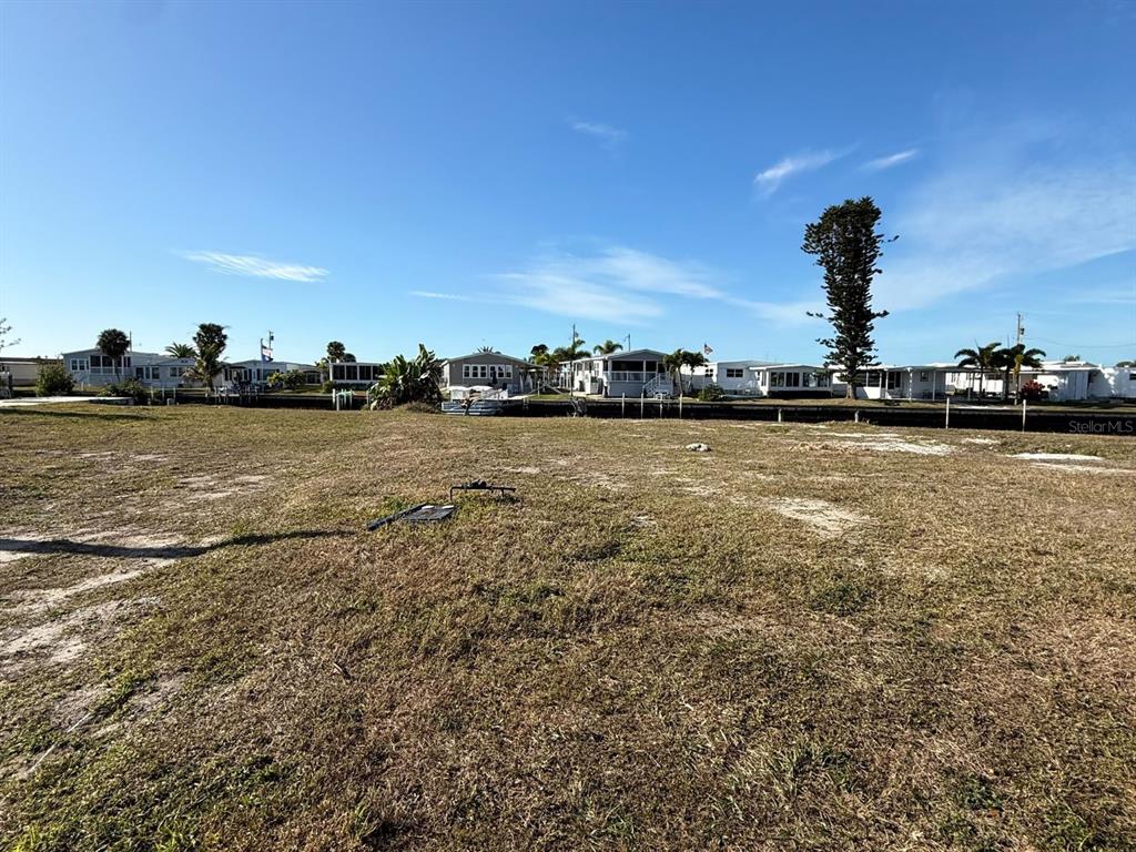 A vacant, grassy lot sits in front of a canal lined with manufactured homes — 506 CLARION PLACE, NORTH PORT, FL