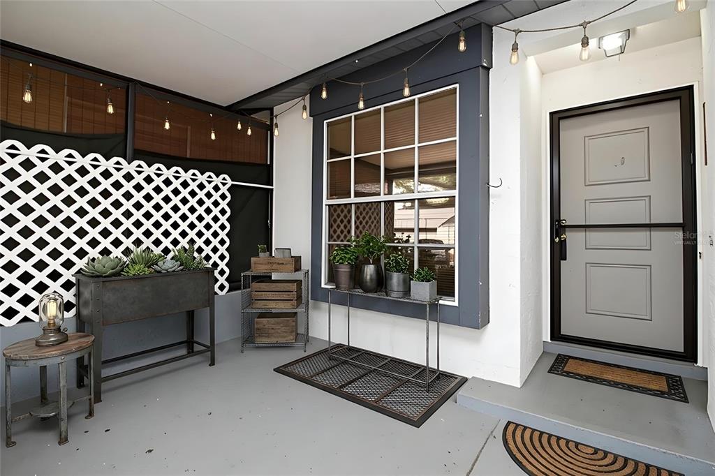 A covered porch features a gray door, a large window, string lights, and potted plants — 7115 PARKSIDE VILLAS DR N, ST PETERSBURG, FL