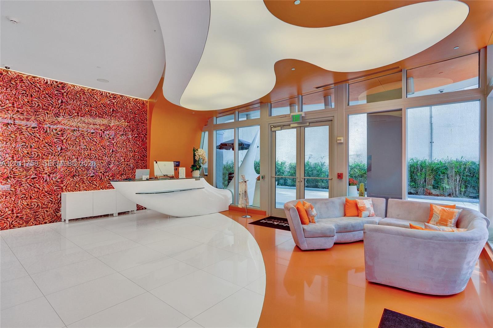 A modern lobby features a white reception desk, orange flooring, and a curved ceiling light — 31 SE 6th St # 805, Miami FL 33131, MIAMI, FL