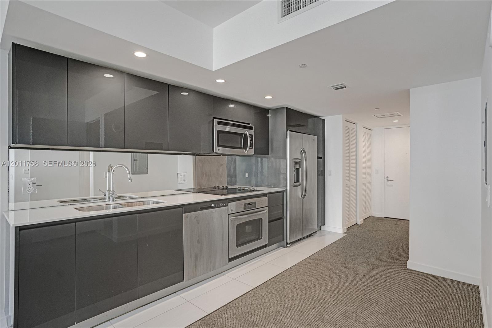 A modern kitchen features dark gray cabinetry, stainless steel appliances, and a mirrored backsplash — 31 SE 6th St # 805, Miami FL 33131, MIAMI, FL