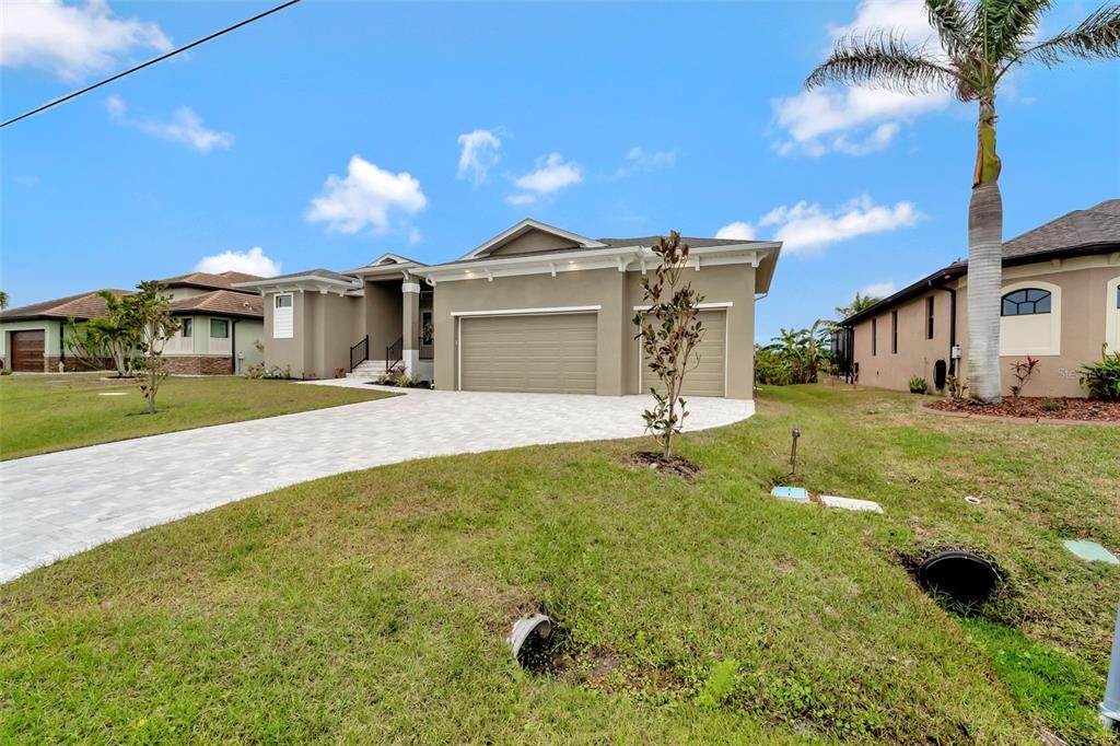 A tan single-story house with a three-car garage and a paved driveway under a blue sky — 10508 MCALESTER CIRCLE, PORT CHARLOTTE, FL