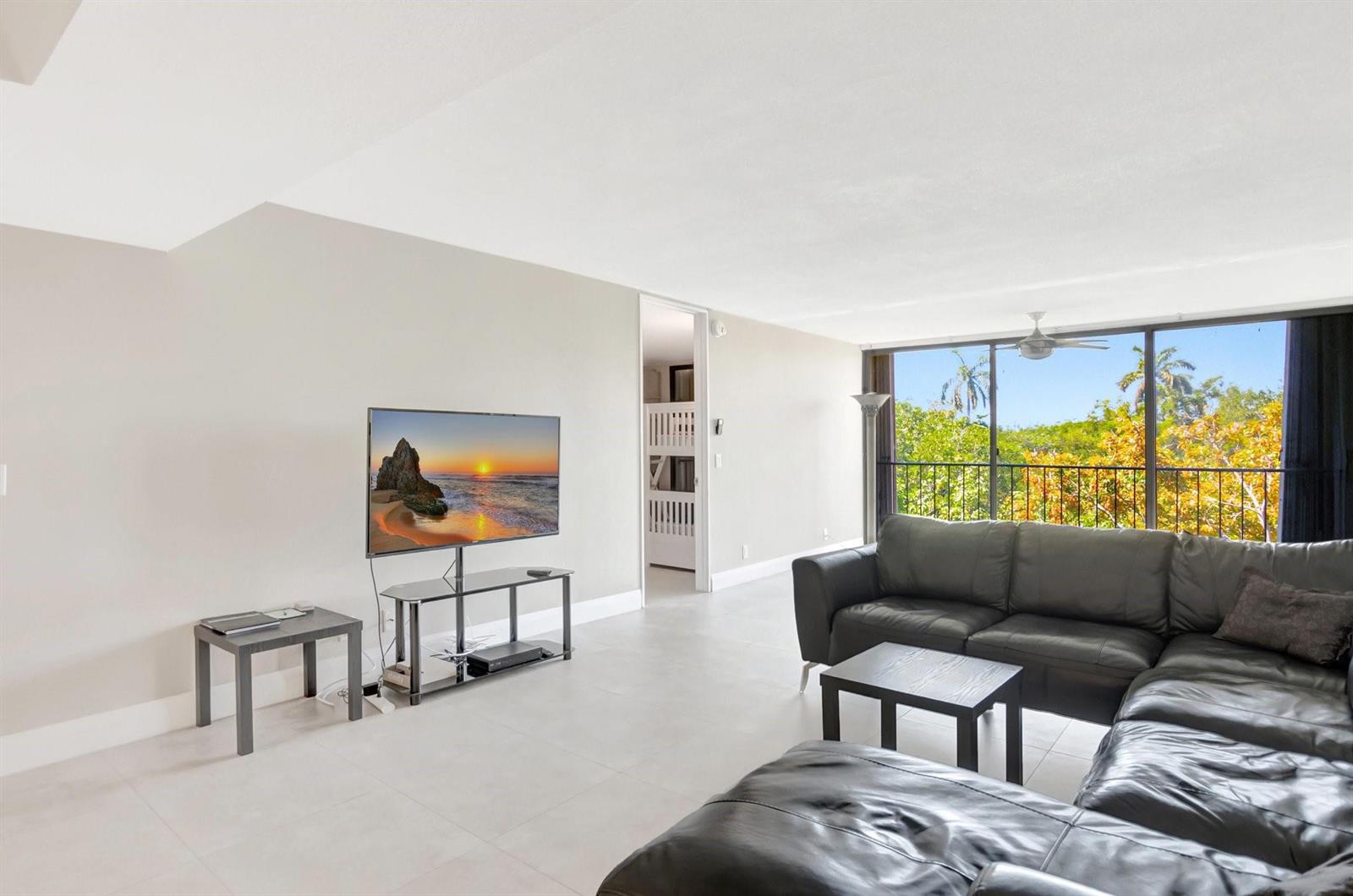 A living room features a black sectional sofa, a television on a stand, and balcony views — 501 SW 11th Place # 403, Boca Raton FL 33432, BOCA RATON, FL