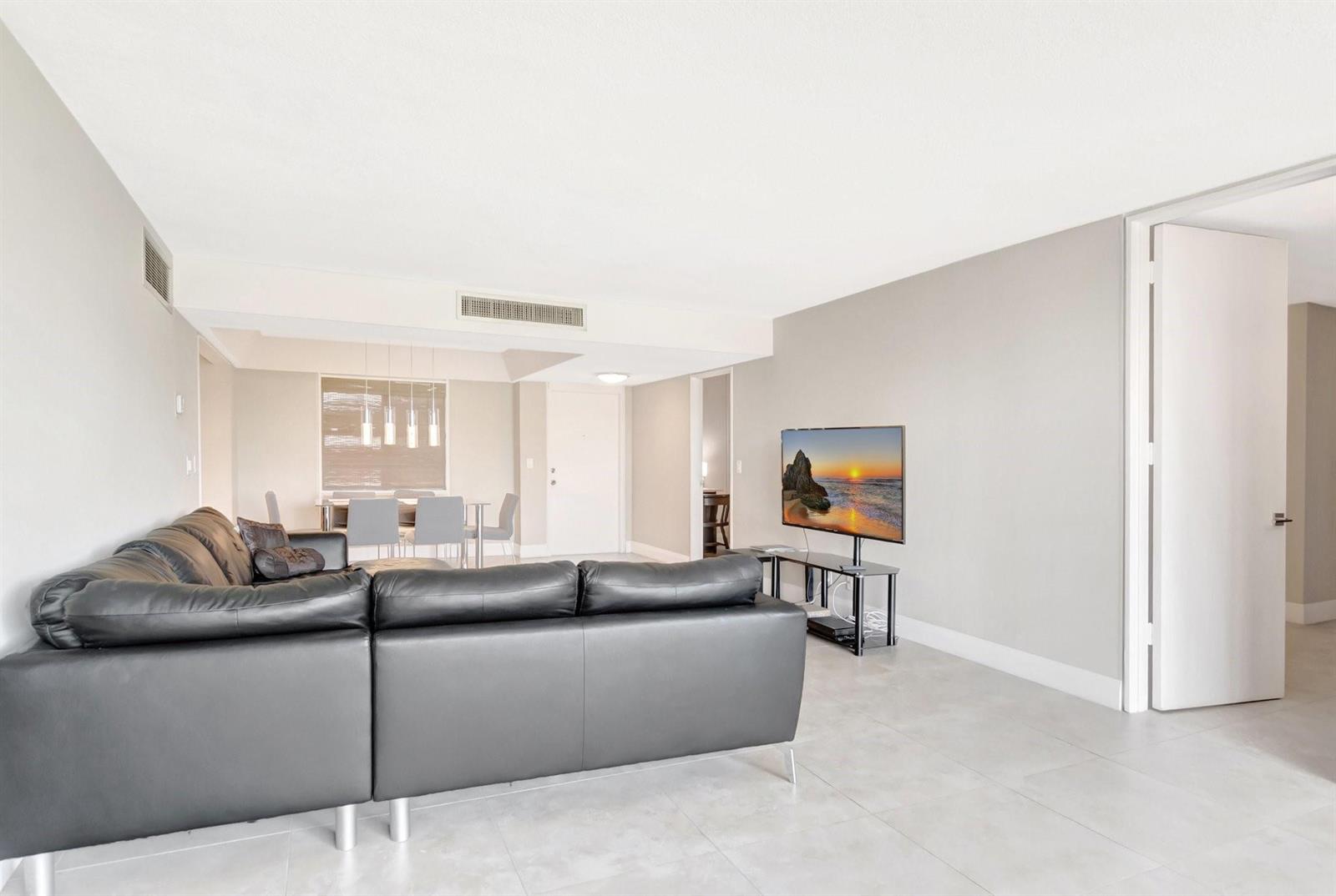 A living room features a black leather sectional sofa, a television on a stand, and tile flooring — 501 SW 11th Place # 403, Boca Raton FL 33432, BOCA RATON, FL