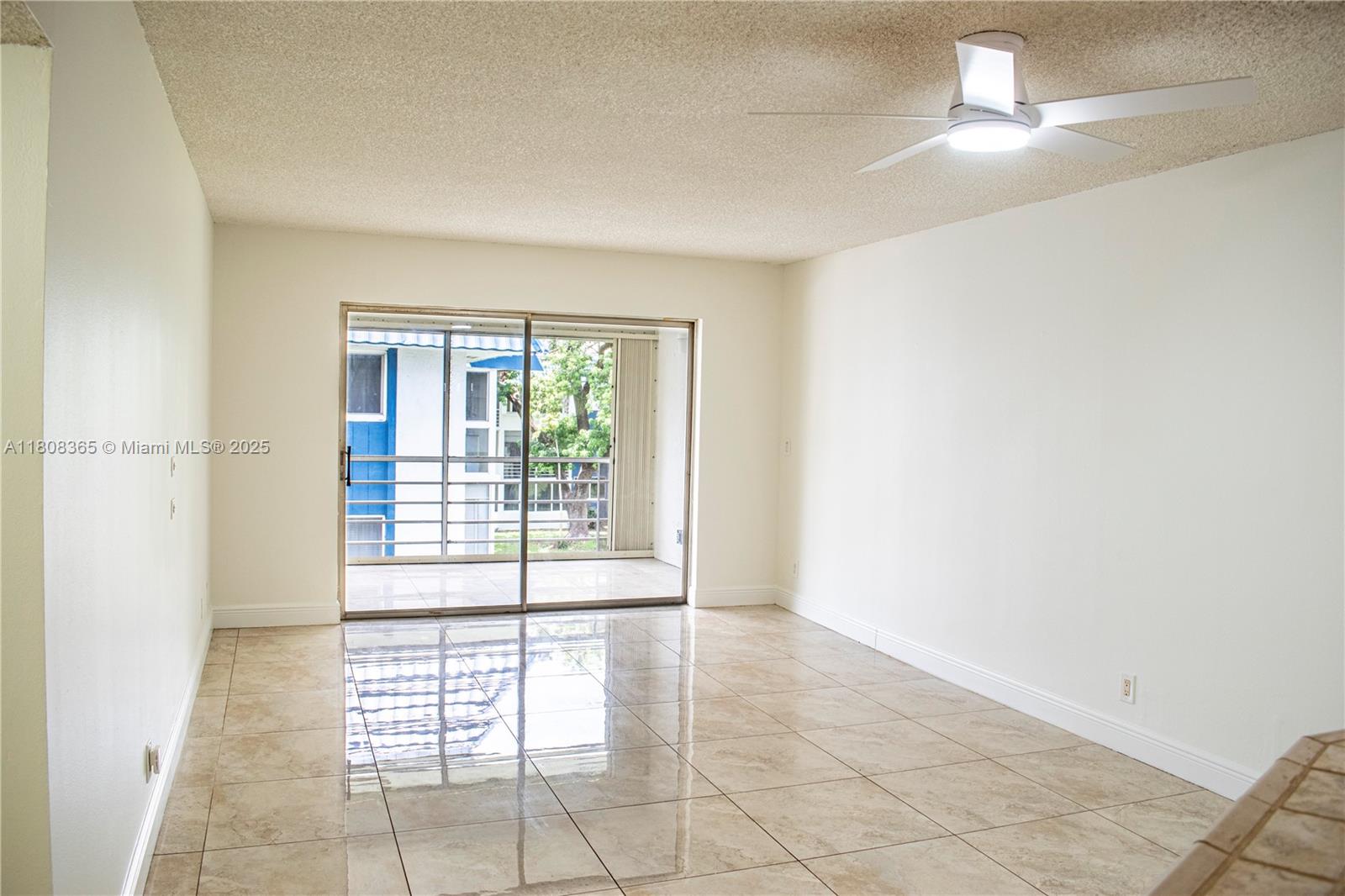 An empty room features beige tile flooring, white walls, a ceiling fan, and a sliding glass door — 3090 Holiday Springs Blvd # 305, Margate FL 33063, MARGATE, FL
