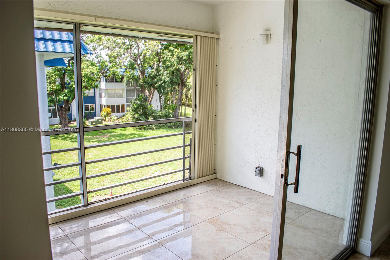 A tiled balcony features a metal railing overlooking a grassy area and trees — 3090 Holiday Springs Blvd # 305, Margate FL 33063, MARGATE, FL