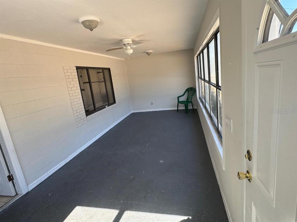 An enclosed porch features a dark painted floor, light walls, a ceiling fan, and windows — 1412 N GARFIELD AVENUE, DELAND, FL